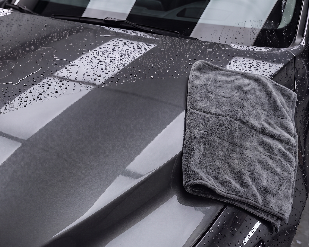 A gloved hand moving a microfiber towel across a wet vehicle panel