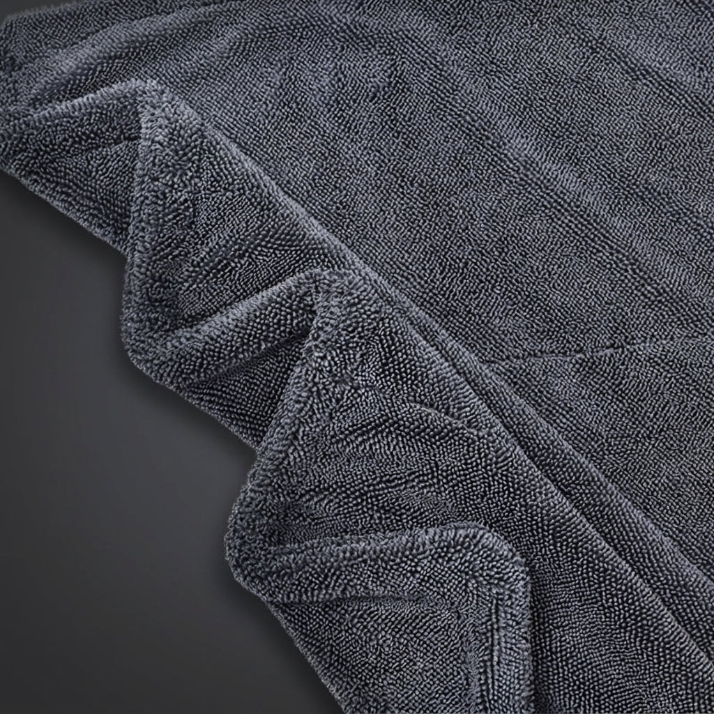 A close-up of a dark gray microfiber or terry cloth fabric, showing its soft, textured surface and folded edges against a dark background.